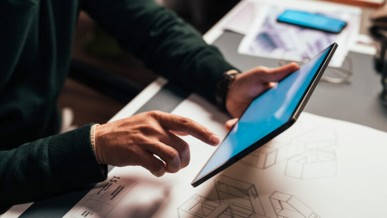 Close-up of a hand interacting with an iPad, with an engineering blueprint in the background